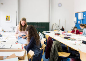 Ein freundlich gestaltetes Klassenzimmer, vereinzelte Schülerinnengruppen arbeiten an Plakaten.