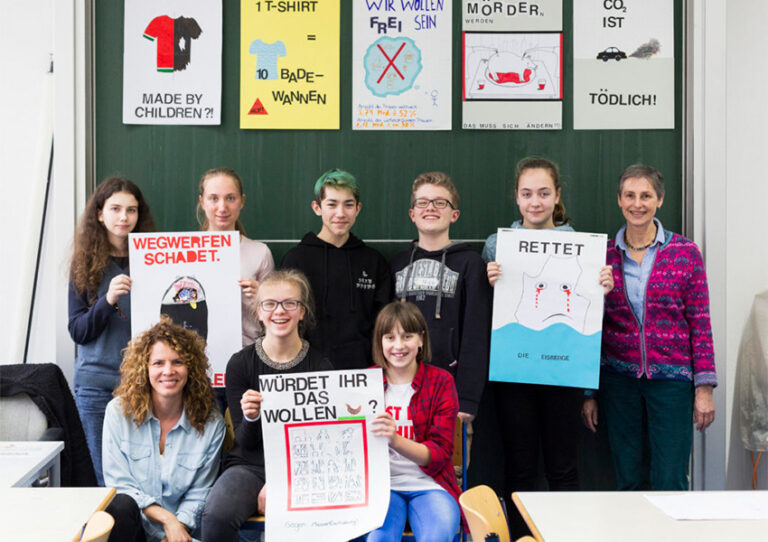 Schüler:innen posieren vor einer Tafel und präsentieren ihre ästhetischen Plakate.