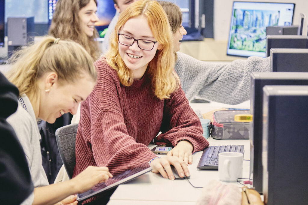 zwei junge fraune an einem tisch in einer schule mit computer und tablet. eine lacht.